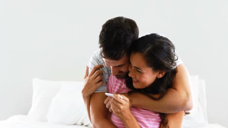 Glückliches-Paar-Schaut-Sich-Den-Schwangerschaftstest-Auf-Dem-Bett-Im-Schlafzimmer-An