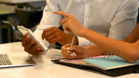 Business-executives-discussing-over-digital-tablet-at-desk