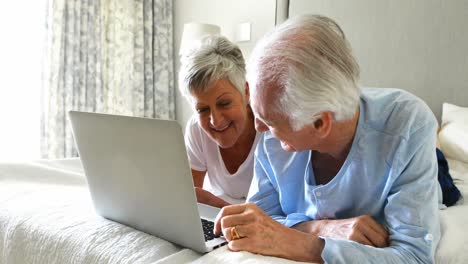 Smiling-senior-couple-using-laptop-on-bed-in-bedroom