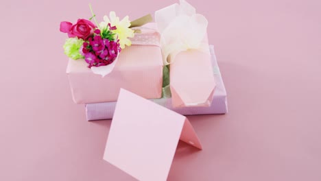 Gift-boxes-with-flowers-and-blank-card-against-pink-background