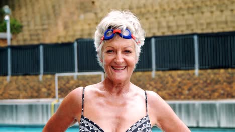 Senior-woman-standing-with-hands-on-hip-near-poolside
