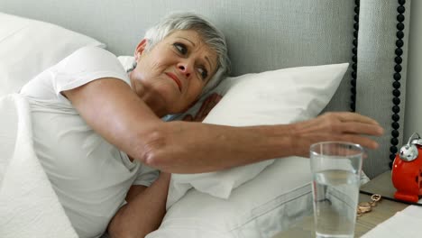Senior-woman-turning-off-alarm-clock-in-bedroom