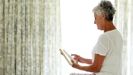 Smiling-senior-woman-reading-book-in-bedroom