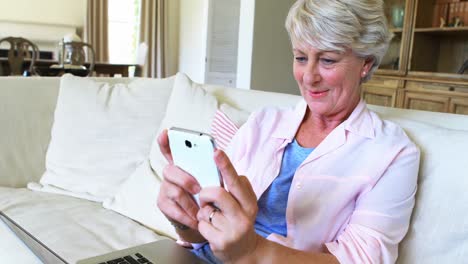 Senior-woman-using-mobile-phone-in-living-room