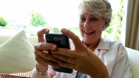Senior-woman-using-mobile-phone-in-living-room
