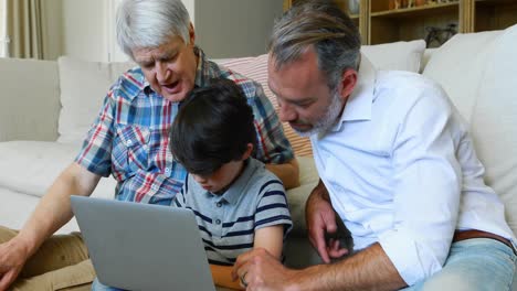 Son,-father-and-grandfather-sitting-on-sofa-using-laptop-in-living-room