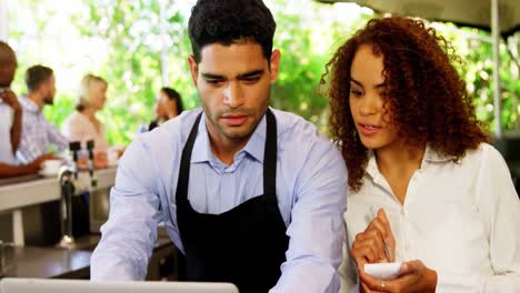 Male-and-female-waiter-discussing-over-laptop
