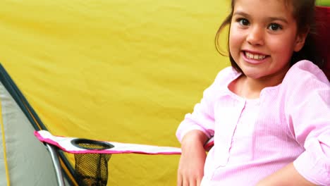 Smiling-girl-sitting-in-chair-by-tent-at-campsite-in-park