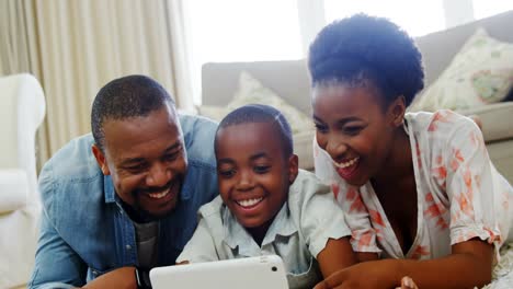 Eltern-Und-Sohn-Liegen-Auf-Dem-Teppich-Und-Nutzen-Ein-Digitales-Tablet-Im-Wohnzimmer