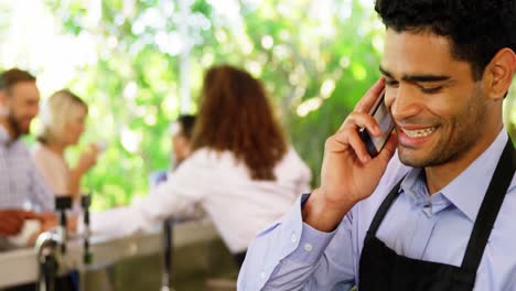 Male-waiter-looking-at-clipboard-while-talking-on-mobile-phone