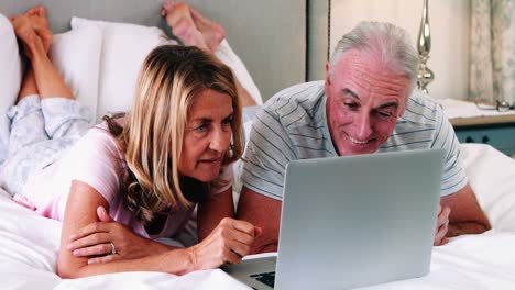 Senior-couple-lying-on-bed-and-using-laptop