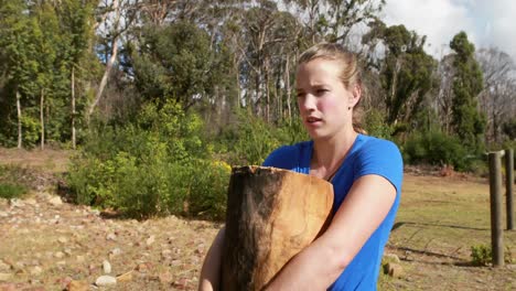 Fit-woman-carrying-heavy-wooden-log-while-exercising
