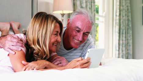 Lächelndes-Paar,-Das-Auf-Dem-Bett-Liegt-Und-Ein-Digitales-Tablet-Benutzt