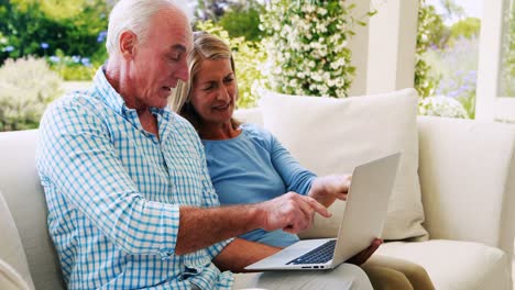 Älteres-Paar-Interagiert-Miteinander,-Während-Es-Im-Wohnzimmer-Einen-Laptop-Benutzt
