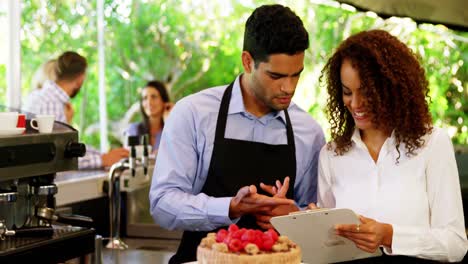 Male-and-female-waiter-discussing-over-clipboard