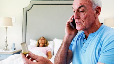 Senior-man-talking-on-mobile-phone-while-senior-woman-resting-in-bedroom