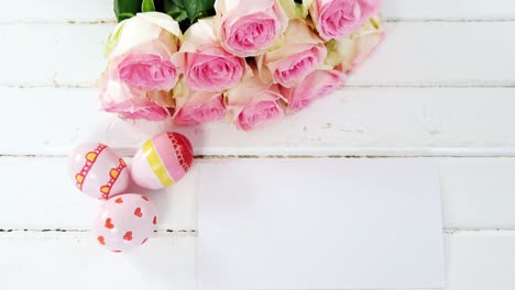 Painted-Easter-eggs,-bunch-of-flower-and-envelope-on-wooden-surface
