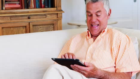 Lächelnder-älterer-Mann-Mit-Digitalem-Tablet-Im-Wohnzimmer