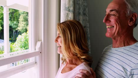 Senior-couple-interacting-with-each-other-while-looking-out-from-the-window