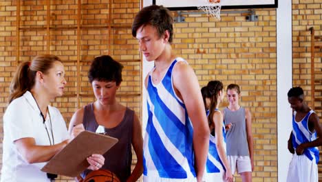 Female-coach-instructing-schoolboys-in-basketball-court