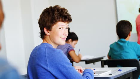 Smiling-schoolboy-doing-classwork-in-classroom