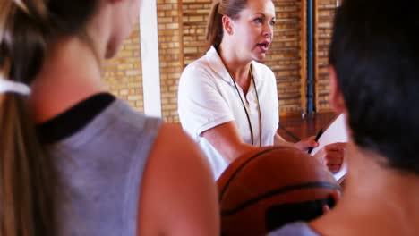 Female-coach-instructing-schoolboys-in-basketball-court
