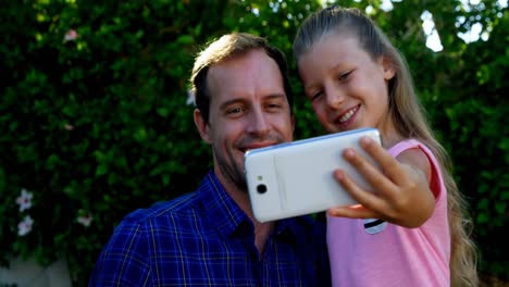 Father-and-daughter-taking-selfie-on-mobile-phone-in-park