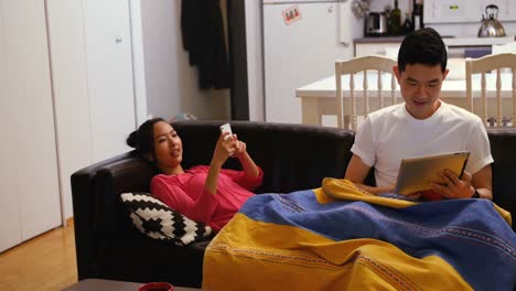 Paar-Entspannt-Sich-Auf-Dem-Sofa-Mit-Digitalem-Tablet-Und-Mobiltelefon-Im-Wohnzimmer