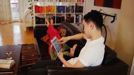 Couple-relaxing-on-sofa-using-digital-tablet-and-mobile-phone-in-living-room