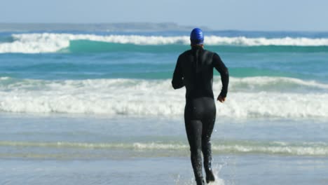 Vista-Trasera-Del-Surfista-Masculino-Corriendo-En-La-Playa