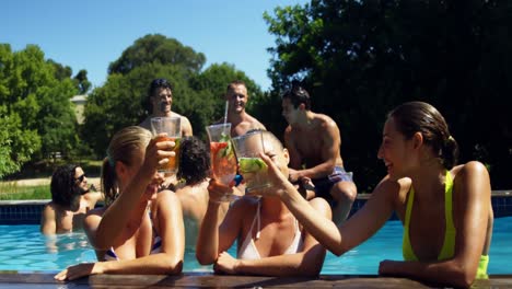 Smiling-womens-toasting-glass-of-cocktails-in-swimming-pool