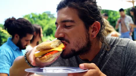 Man-eating-hamburger-at-outdoors-barbecue-party