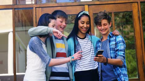 Smiling-schoolkids-looking-photos-on-mobile-phone