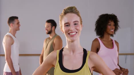 Beautiful-woman-smiling-while-her-group-talking-in-background-in-fitness-studio