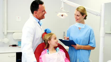 Dentist-interacting-with-nurse-while-treating-to-girl