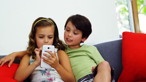 Siblings-using-mobile-phone-in-living-room