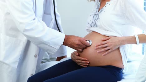 Doctor-Examinando-El-Vientre-De-Una-Mujer-Embarazada-Con-Un-Estetoscopio-En-La-Sala.