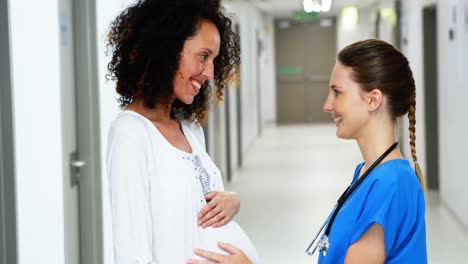 Doctor-touching-pregnant-womans-belly-in-corridor