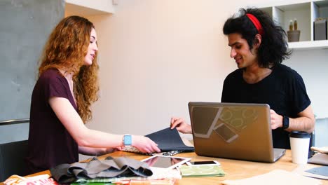 Executives-using-laptop-while-examining-fabric