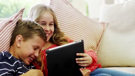 Siblings-using-digital-tablet-in-living-room