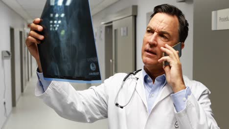 Male-doctor-talking-on-mobile-phone-while-talking-on-mobile-phone-in-corridor
