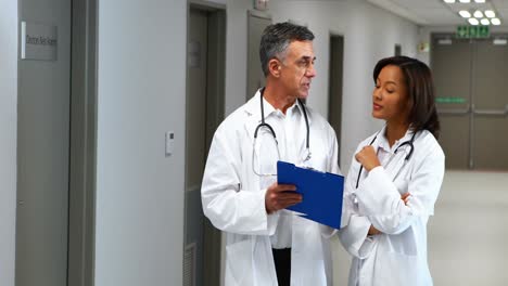 Doctors-having-discussion-over-clipboard-in-corridor