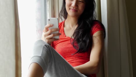 Woman-sitting-on-windowsill-and-using-mobile-phone