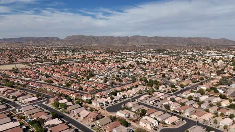 Aerial-View-of-Suburbs-in-Arizona,-Hundreds-of-Family-Homes-with-Mountain-Range-and-Blue-Sky-in-Background