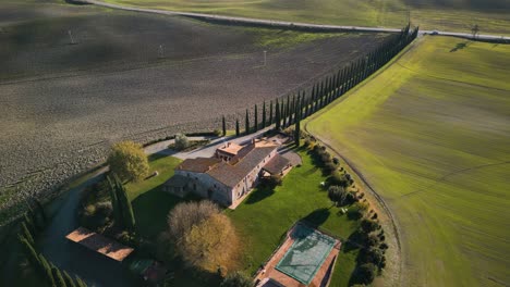 Descripción-Aérea-Cinematográfica-De-Una-Mansión-En-Lo-Alto-De-Una-Gran-Granja-Agrícola-Con-Vibrantes-Tierras-Verdes,-Val-D&#39;orcia-Toscana