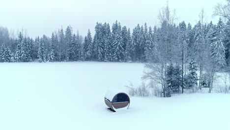 Aerial-modern-round-wood-cabin-in-the-woods-with-snow-on-spruce-tree,-Riga-Latvia