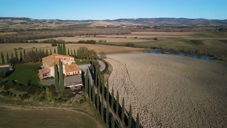 Drone-pulls-back-from-orange-roof-stone-mansion-overlooking-dry-and-lush-grass-landscape