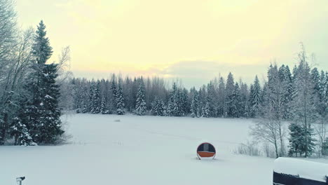 Pullback-aerial-reveal-of-a-sauna-and-trailer-cabin-in-a-countryside-winter-landscape