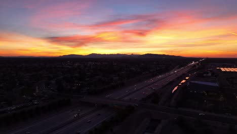 Aerial-View-of-Busy-Highway-in-Late-Evening-with-Colorful-Sunset-over-Mountain-Range