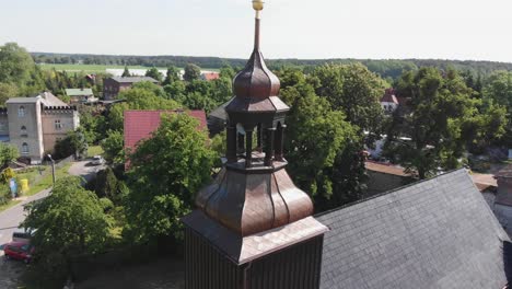 Aerial-orbit-of-intricate-dark-wood-bell-tower-as-birds-soar-in-air-of-rural-village